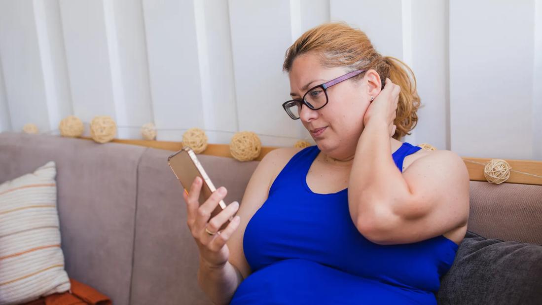 Person with overweight sitting on couch looking at phone