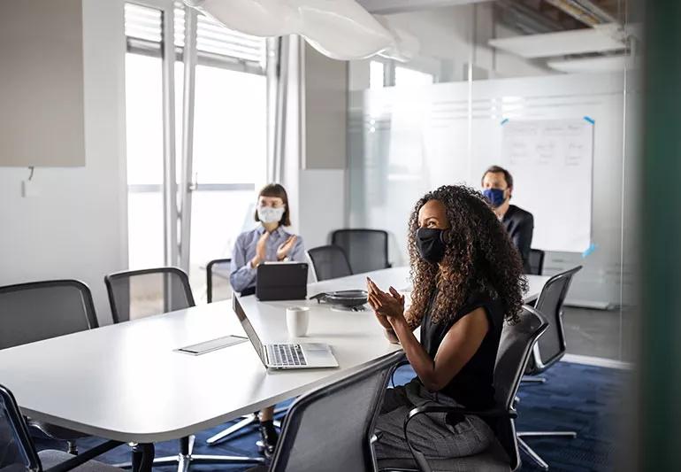 Three people with masks sitting in a conference room.