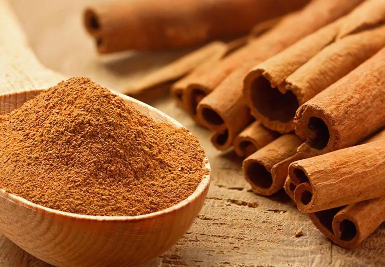 A small wooden spoon brimming with cinnamon alongside a pile of cinnamon sticks