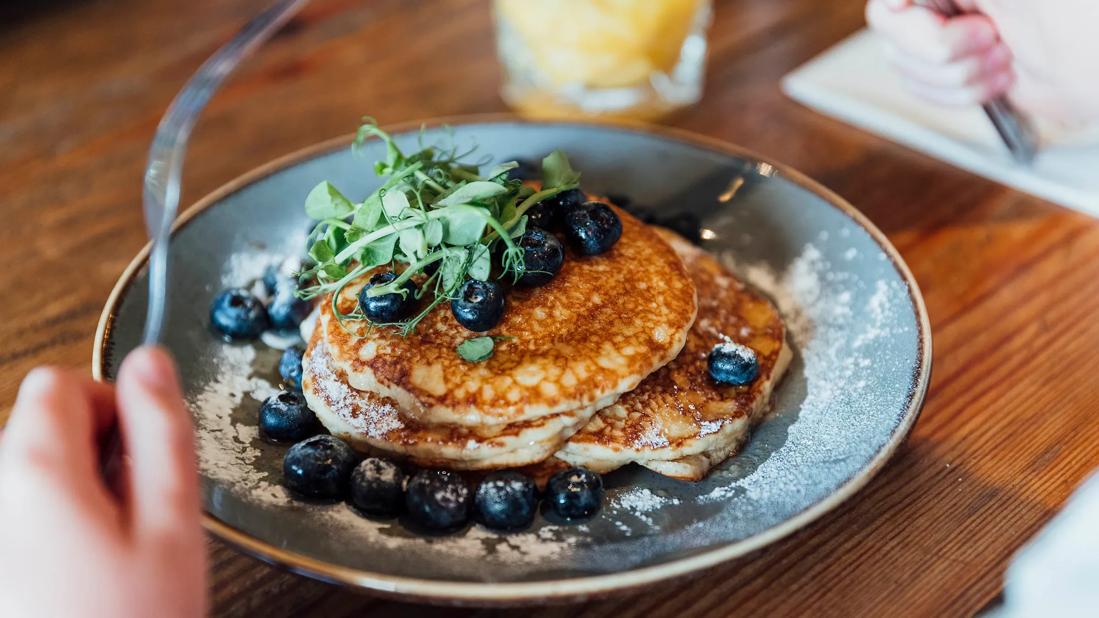 Person about to eat a plate full of pancakes with blueberries on top