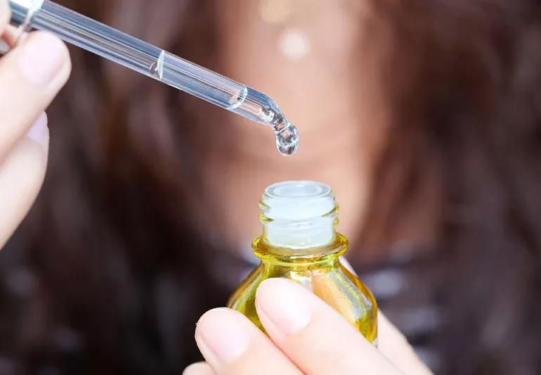 Closeup of person holding vitamin C serum, with dropper filled with liquid.