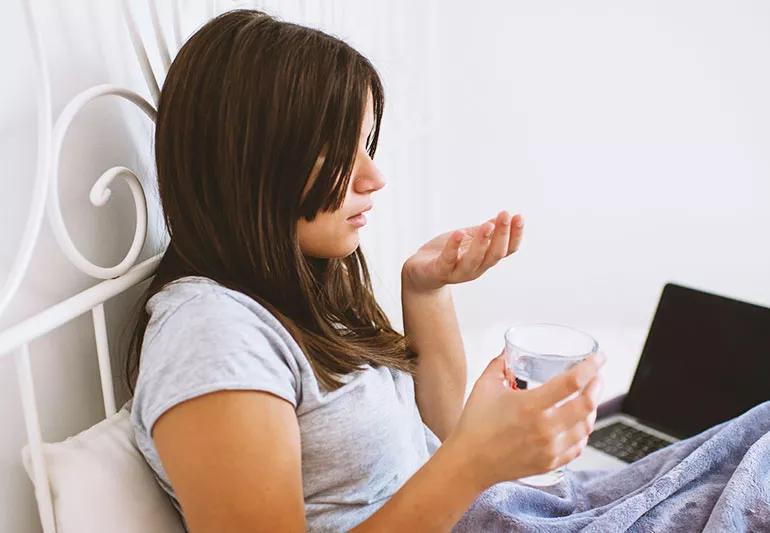 A teenager prepares to take some Benadryl with a glass of water.