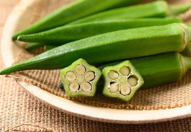 Closeup of okra in wooden bowl, both uncut and some star-shaped wedges.