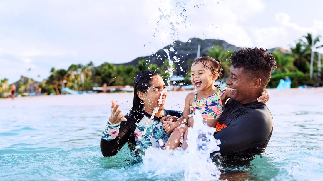 Caregivers holding toddler, playing in ocean