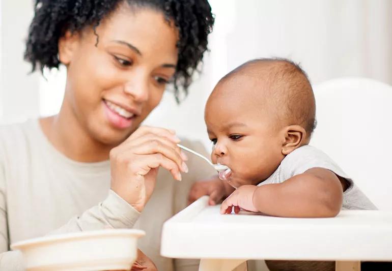 mother feeding baby sitting in high chair