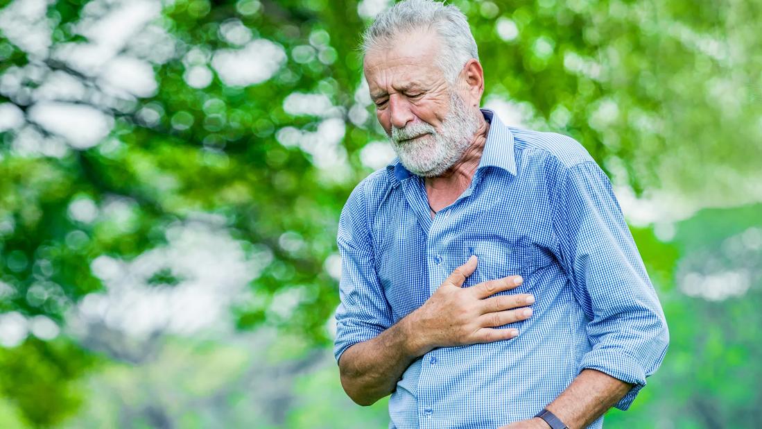 Older man walking outside, grimacing, clutching their chest