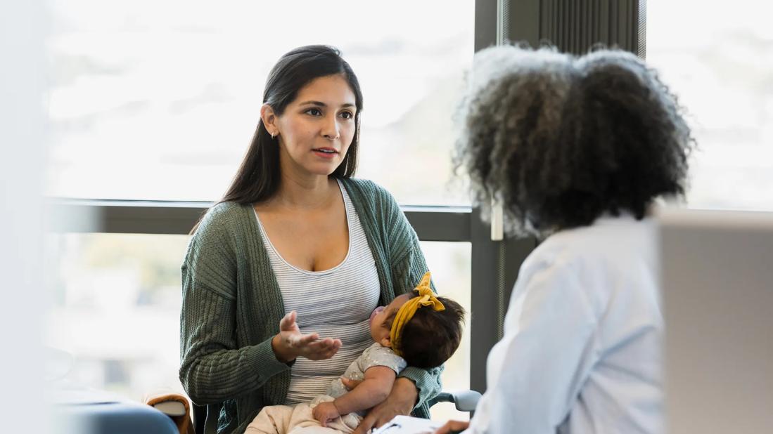 Caregiver holding baby while talking with a healthcare provider in medical office