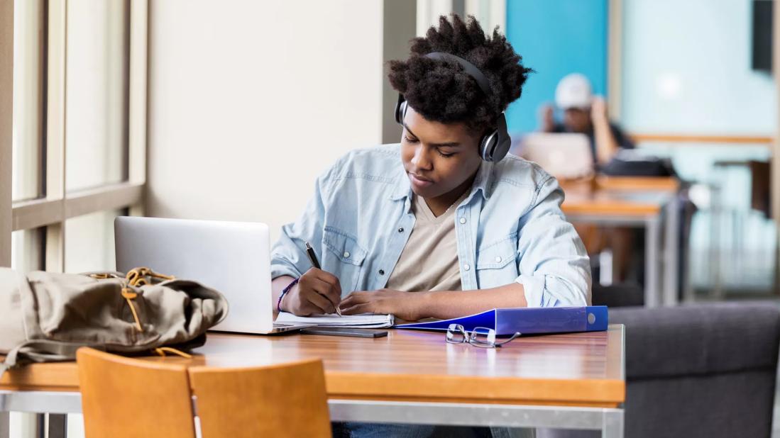 Person studying with headphones on, with laptop and notepad