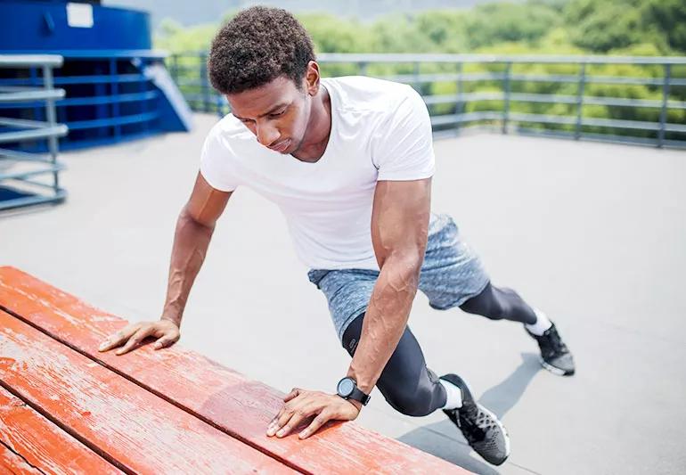 A person in workout clothes stretching their hips by holding onto a table and rotating torso