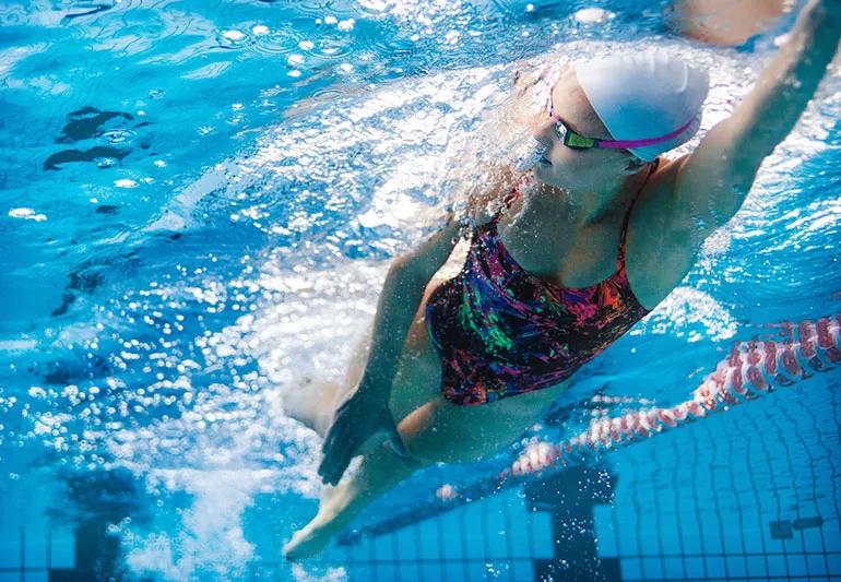 Person in pool swimming freestyle down a lane.