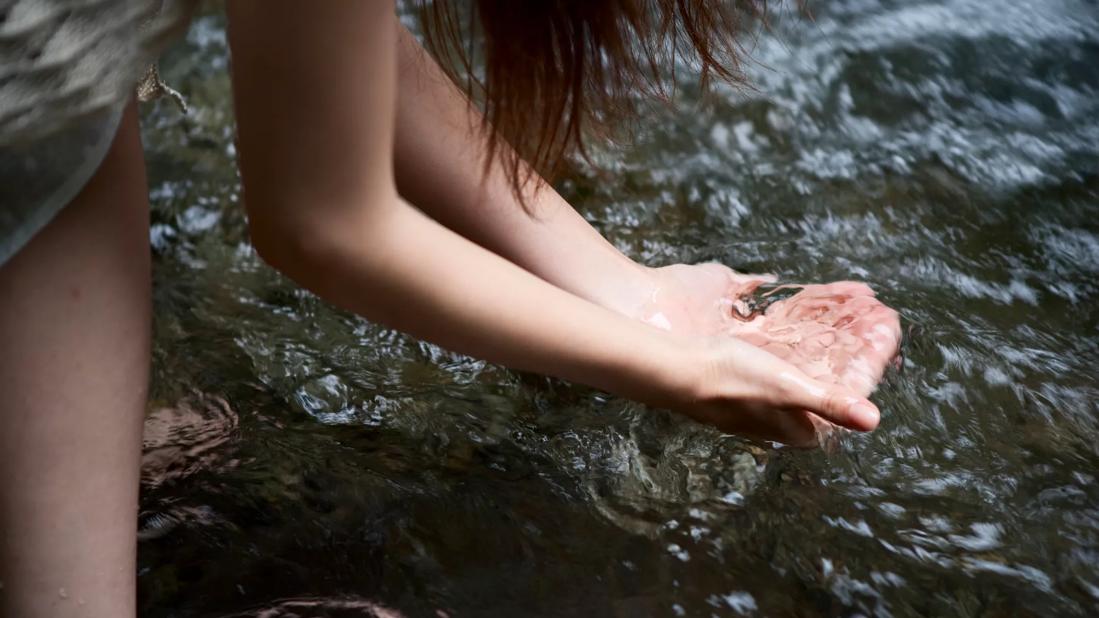 Person scooping up water in hands from creek