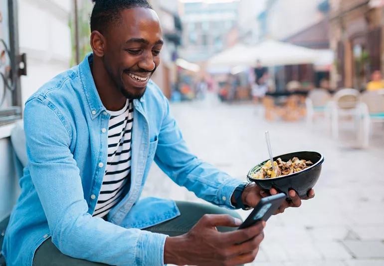 Person enjoying taco in a bowl at a street fair while talking on phone.