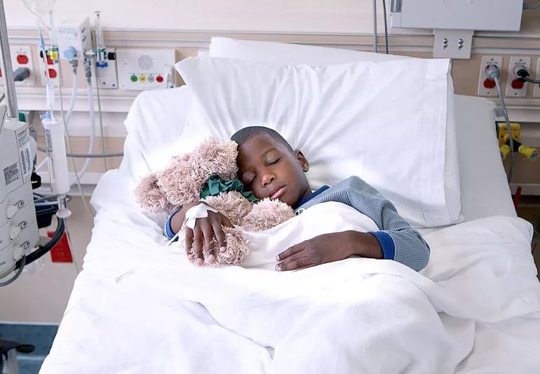 child hugging stuffed bear in hospital bed
