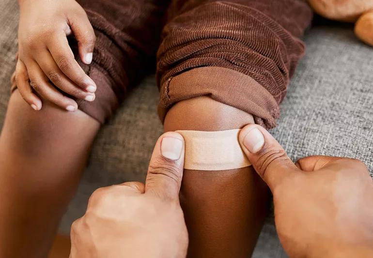 Closeup of Parent putting bandaid on child's hurt knee.