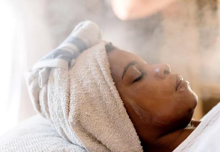 woman with hair towel at spa steaming her face