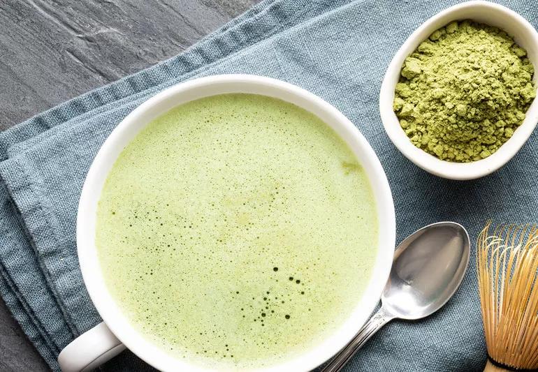 A cup of frothy green tea in foreground and powdered matcha in background.