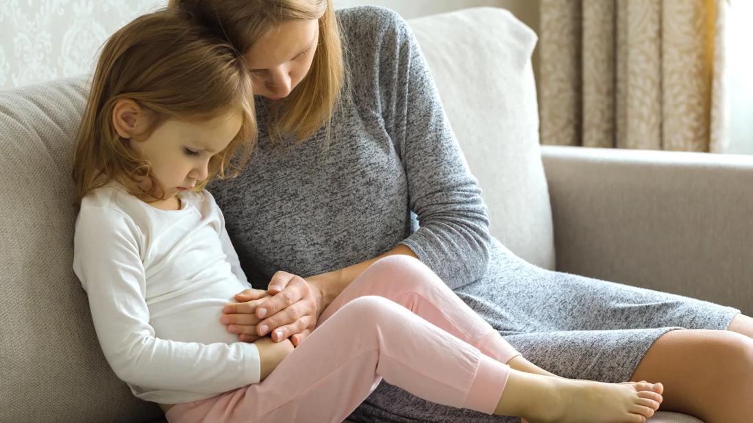 Child with mom sitting on couch with hands on the child's stomach