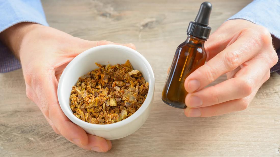 Hands holding small bowl of propolis and dropper bottle of liquid propolis