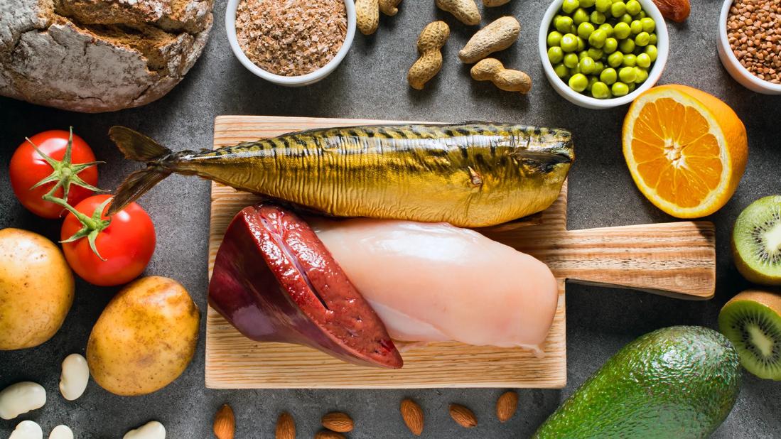 Stone table with niacin-rich foods, like nuts, avocado, tomatoes, and cutting board with raw liver, chicken and fish