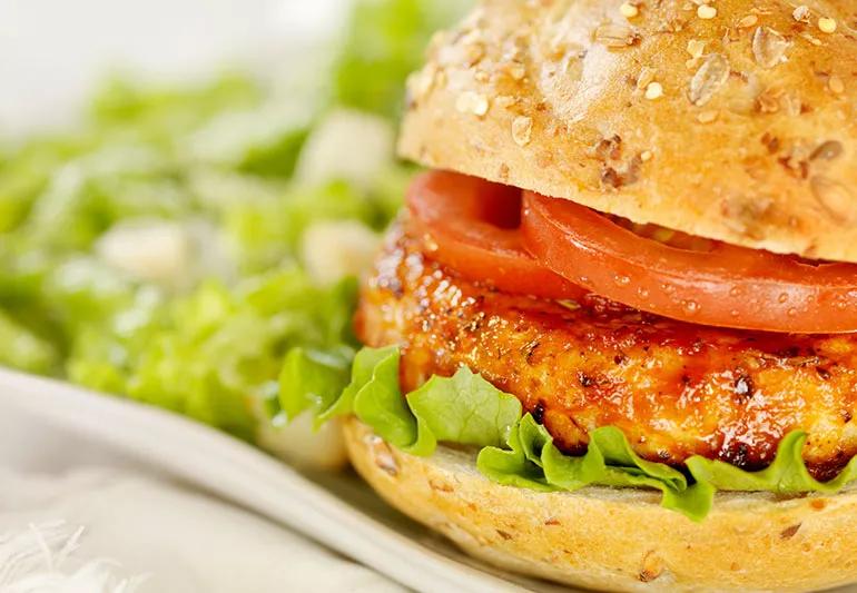 A close-up of a grilled turkey burger on a wheat bun with sliced tomato and leafy lettuce