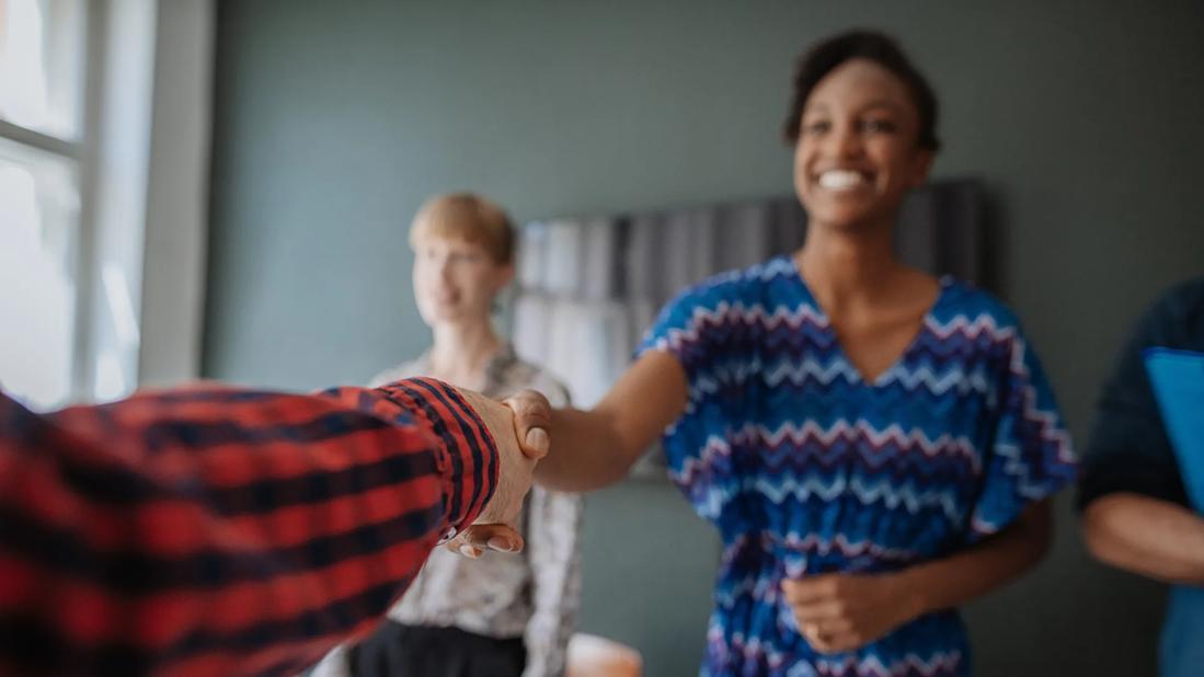 People standing, shaking hands across table from each other