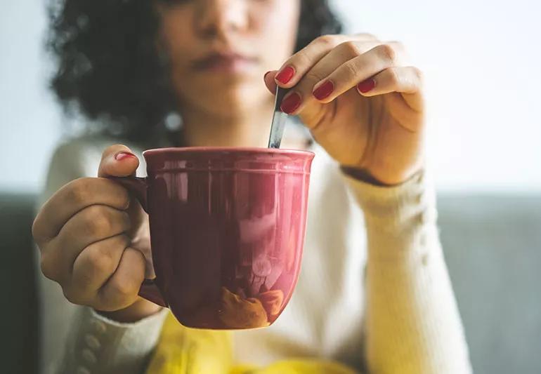 Coffee mug in foreground with person in background holding it.