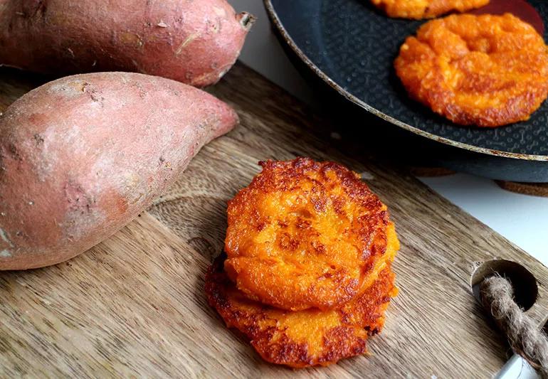A couple of raw sweet potatoes are displayed next to a plate of small, crisp, ginger sweet potato pancakes.