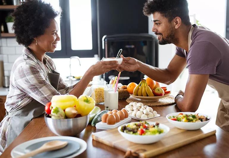 A couple cook a healthy meal in the kitchen while stopping to share a coffee during the process.