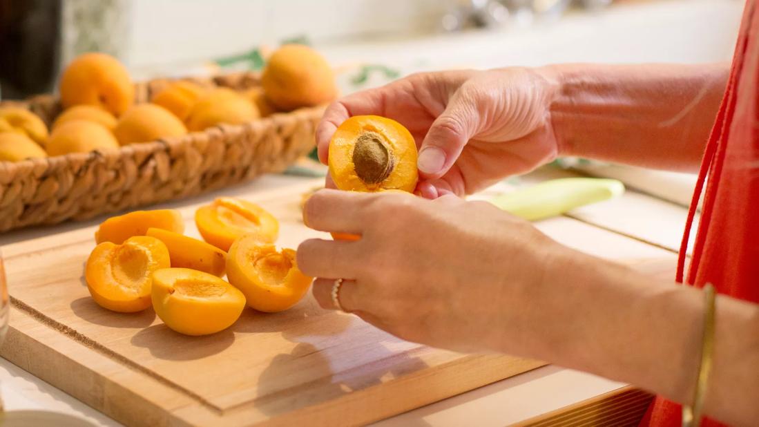 Person halving apricots and removing pits on cutting board