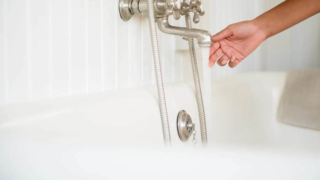 Hand testing water temperature from bathtub faucet