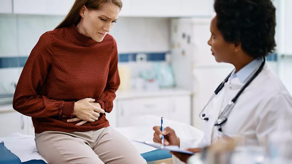 patient in doctor's office clutches stomach while provider takes notes