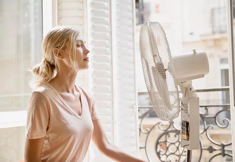 young lady sitting in front of standing fan to cool down