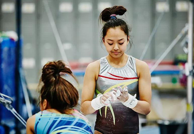 Young gymnast puts chalk on hands in a gym setting