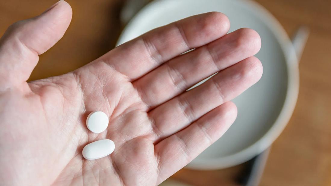 Open palm holding a white round pill and a white oblong tablet