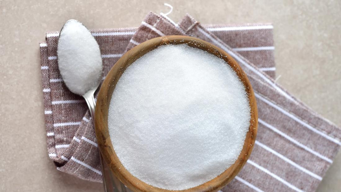 Artificial sweetener in wooden bowl on kitchen towel, with spoonful nearby