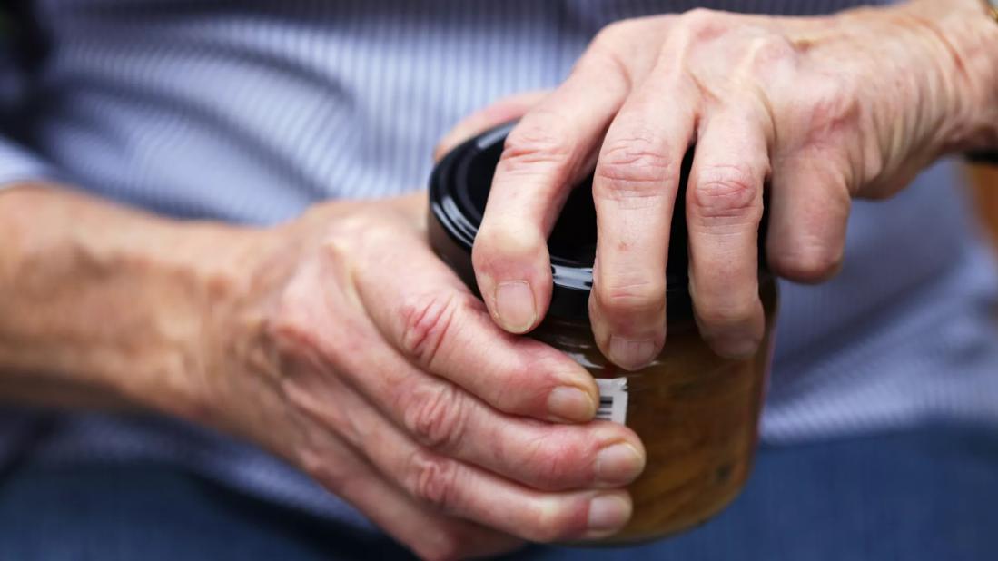 Close up of hands with swollen joints twisting a lid off a jar.