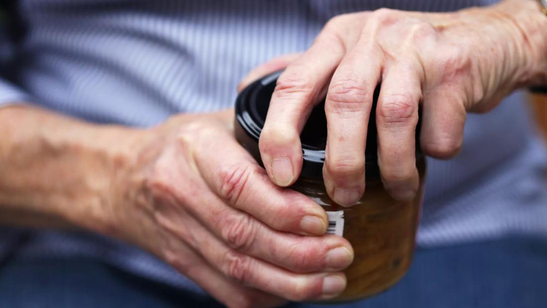 Close up of hands with swollen joints twisting a lid off a jar.