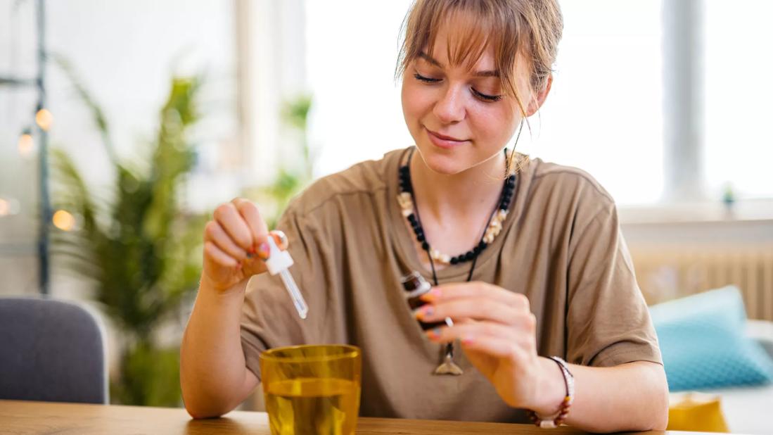 Person holding bottle and dropper, adding droplets into glass of water