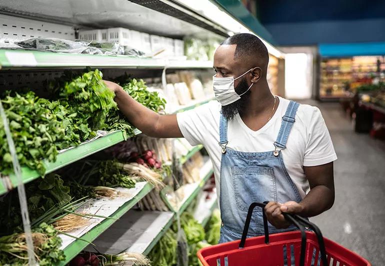 man picking lettuce from shelf at grocery store during pandemic