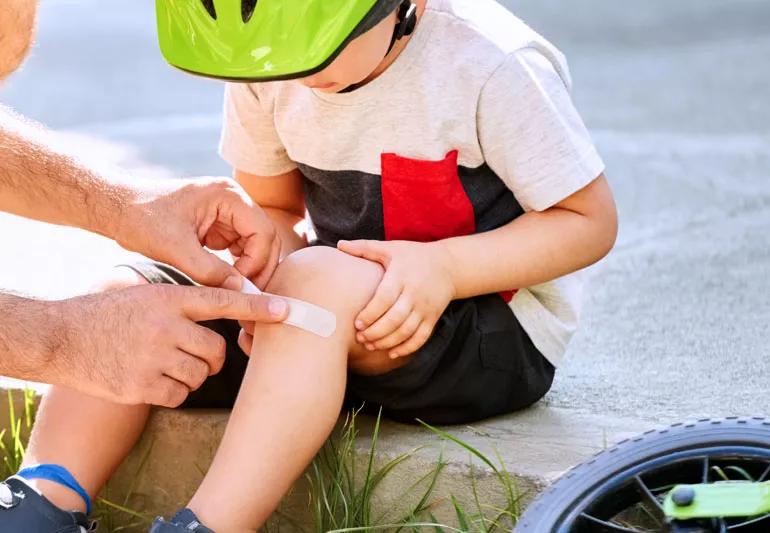 man applies bandage to child's knee