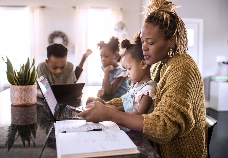 Busy mom helps children with homework while holding baby, working on computer and talking on phone.