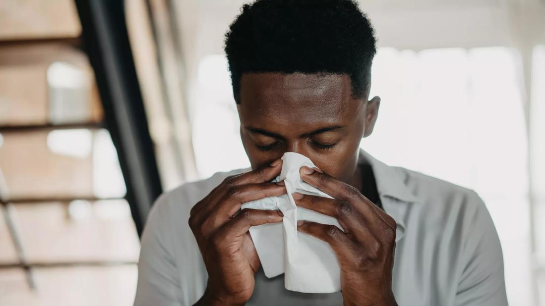 Adult male hunched over blowing his nose into a tissue