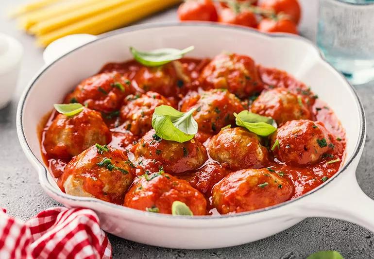 A white bowl of meatballs in a red marinara sauce
