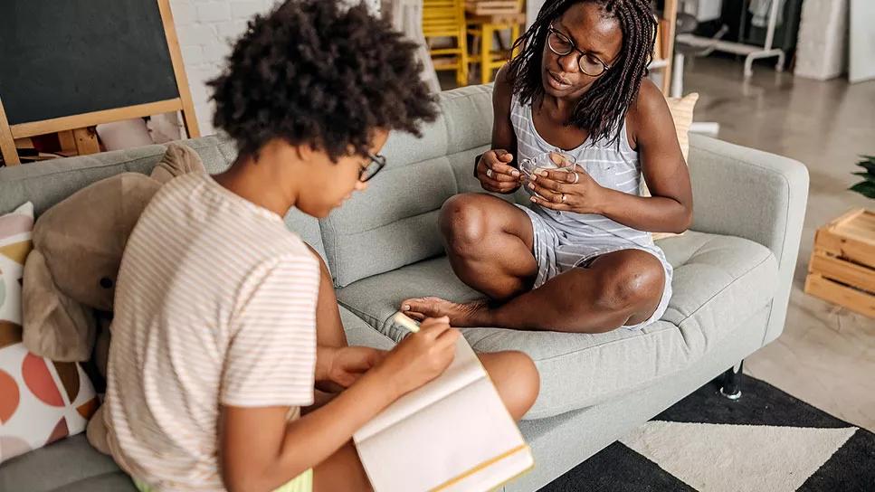 Teenager and parent work on homework together on couch at home