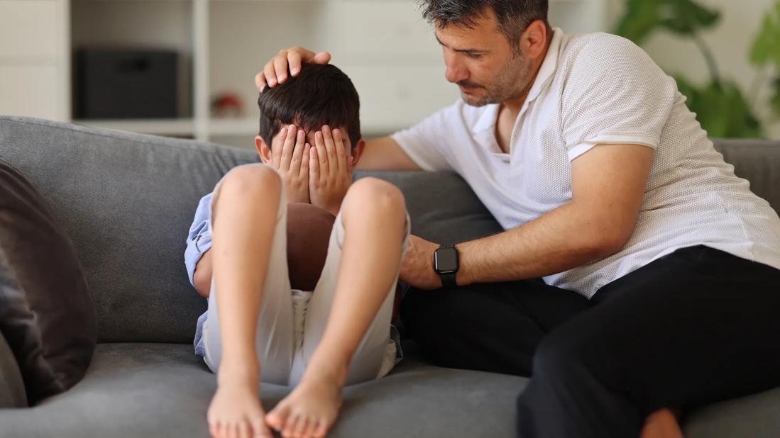 Caregiver sitting with and consoling an upset child on a couch