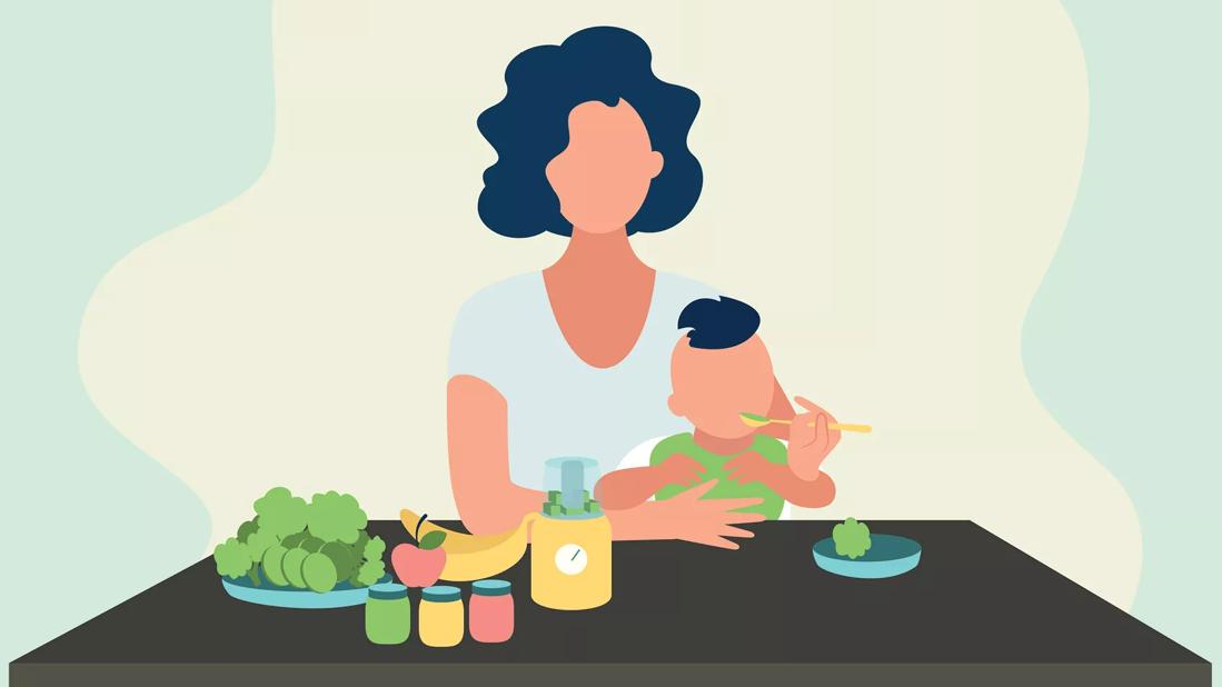 A person sits at a table with food and feeds their baby with a spoon