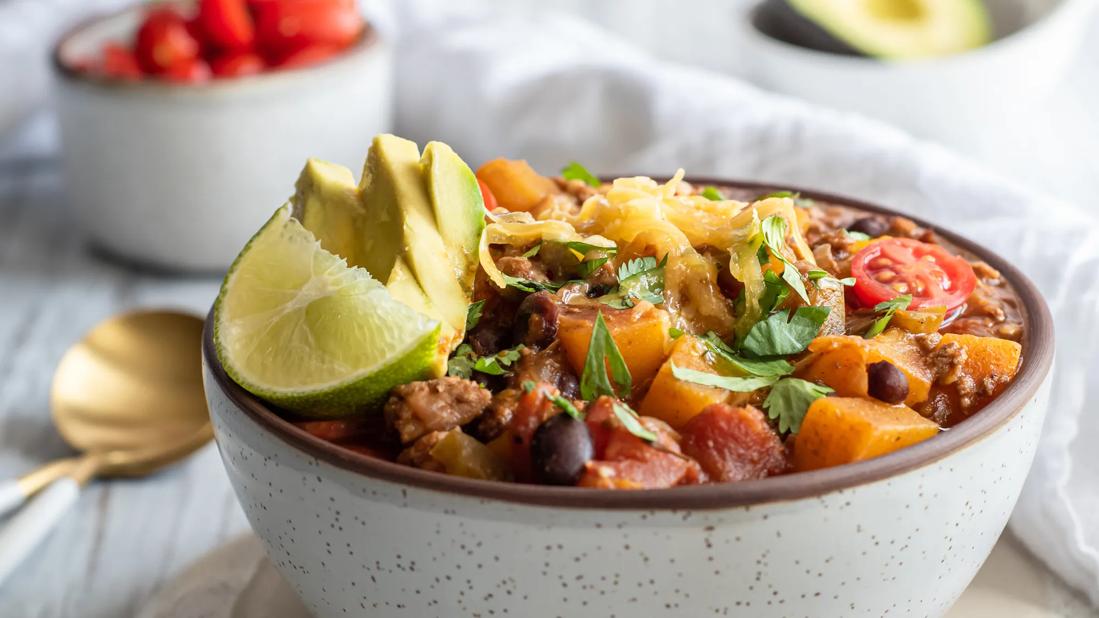 A bowl of chili with chunks of butternut squash, with lime wedge garnish