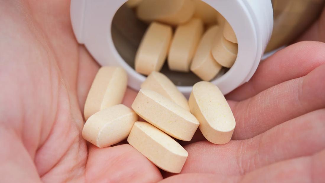 Tan tablets pouring from bottle into a hand