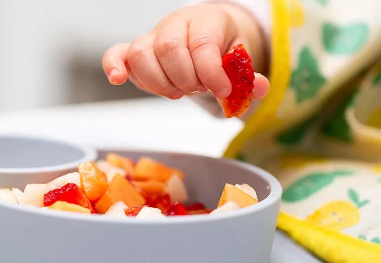 baby eating fruit that is cut up into small pieces