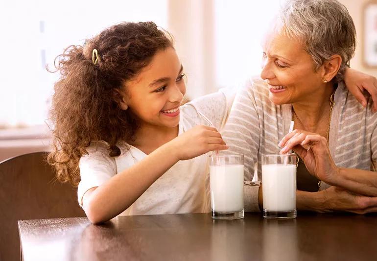 Grandmother and granddaughter enjoying glasses of milk or soy milk